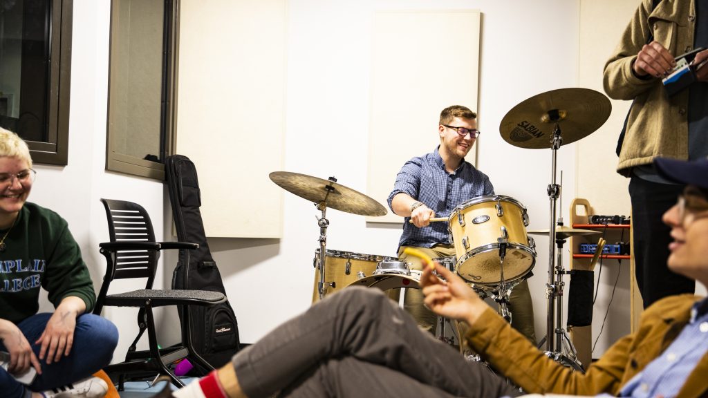 Group of students in a room playing drums and sitting on couches